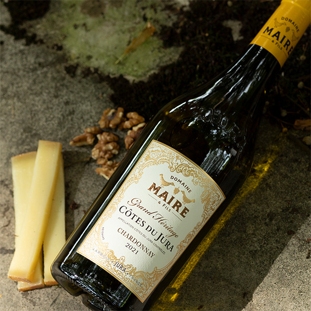 Vins & Délices Bouteille d'Arbois sur un Tonneau accompagné de morceaux de noix et de tranches de Comté